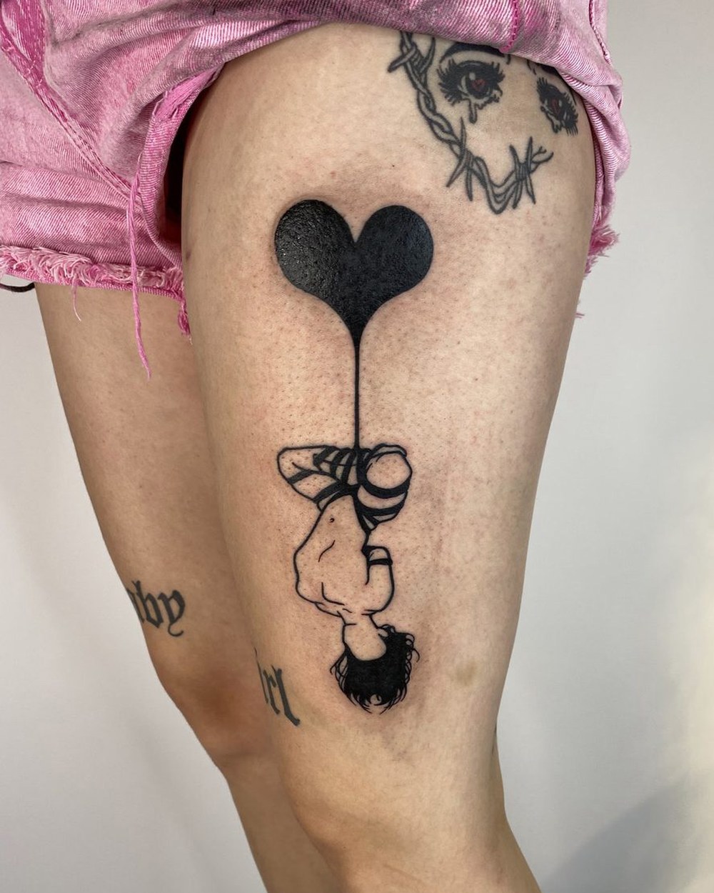 Blackwork heart-shaped balloon on a bunch of string, tattooed on a thigh